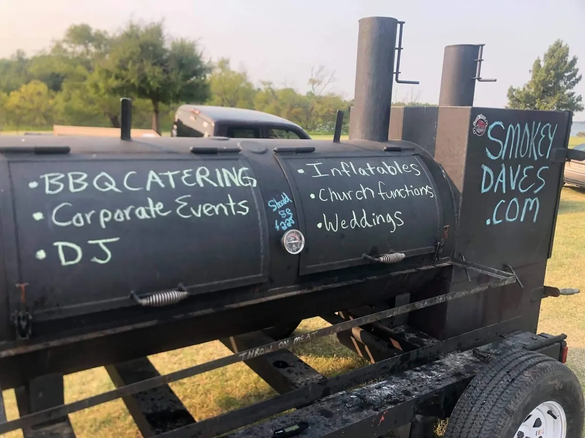 Trinity smoker trailer with chalkboard listing BBQ catering, corporate events, DJ, inflatables, church functions and weddings